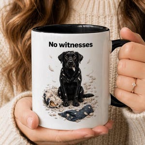 May include: White ceramic mug with a black interior and handle. The mug features a black Labrador illustration with the text "No witnesses". The dog is sitting on a sandy surface.