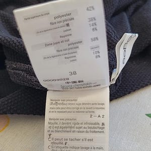 May include: A close-up of a clothing tag with text in French. The tag lists fabric composition percentages, including polyester, rayon, and cotton. The number 38 is visible, along with care instructions.