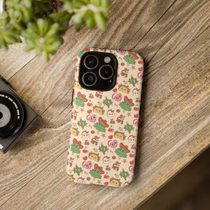 May include: A phone case with a repeating pattern of cartoon tacos, cacti, and other festive elements in red, green, and yellow on a beige background. The case is on a wooden surface.