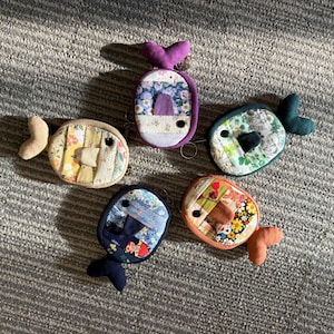 May include: Five handmade fish-shaped coin purses in various colors and patterns. Each purse features a unique fabric design, including floral and patchwork motifs. The fish have button eyes and fabric fins, with a key ring attached.
