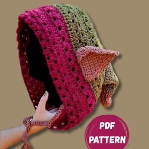 May include: A crocheted hood featuring a deep magenta front border and an olive green main section. The hood includes two pointed, light brown ears on the side and thin crocheted ties at the chin. A circular graphic displays the text PDF PATTERN.