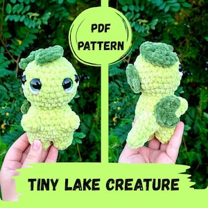 Può includere: Un peluche all'uncinetto di una piccola creatura del lago in filato verde chiaro con accenti verde scuro, grandi occhi neri e una coda. L'immagine include il testo PDF PATTERN e TINY LAKE CREATURE, mostrando le viste frontale e posteriore.