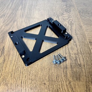 May include: A black, geometric bracket with a triangular design and several screw holes. A small group of silver screws is next to the bracket. The bracket is on a wooden surface.