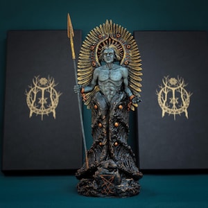 Puede incluir: Una estatua humanoide de tonos grises con un halo dorado, sosteniendo una lanza alta en la mano derecha. La figura presenta una prenda inferior oscura y texturizada con detalles dorados, sobre una base marcada con un sigilo rojo.