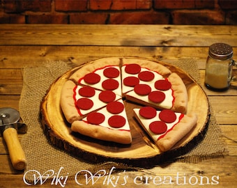 May include: A felt pizza with pepperoni and cheese toppings on a wooden cutting board. The pizza is cut into slices and there is a pizza cutter on the table.