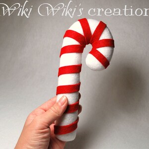May include: A white and red felt candy cane ornament. The candy cane is about 12 inches long and has a red and white striped pattern.