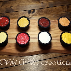 May include: Eight small black bowls filled with different colored sauces on a wooden board. The sauces are red, yellow, orange, white, and a darker red.