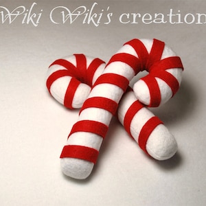May include: Two red and white striped felt candy canes. The candy canes are crossed over each other.