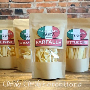 May include: Three brown paper bags with clear plastic windows, each containing a different type of dried pasta. The bags are labeled with the text "Wiki's Pasta" and the names of the pasta types: "Penne", "Ravioli", "Farfalle", and "Fettuccine".