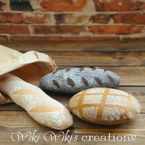 May include: Three felt loaves of bread on a wooden surface. The loaves are a light brown, dark brown, and a tan color. The loaves are decorated with different patterns. The text "Wiki Wiki's creations" is visible in the bottom right corner of the image.