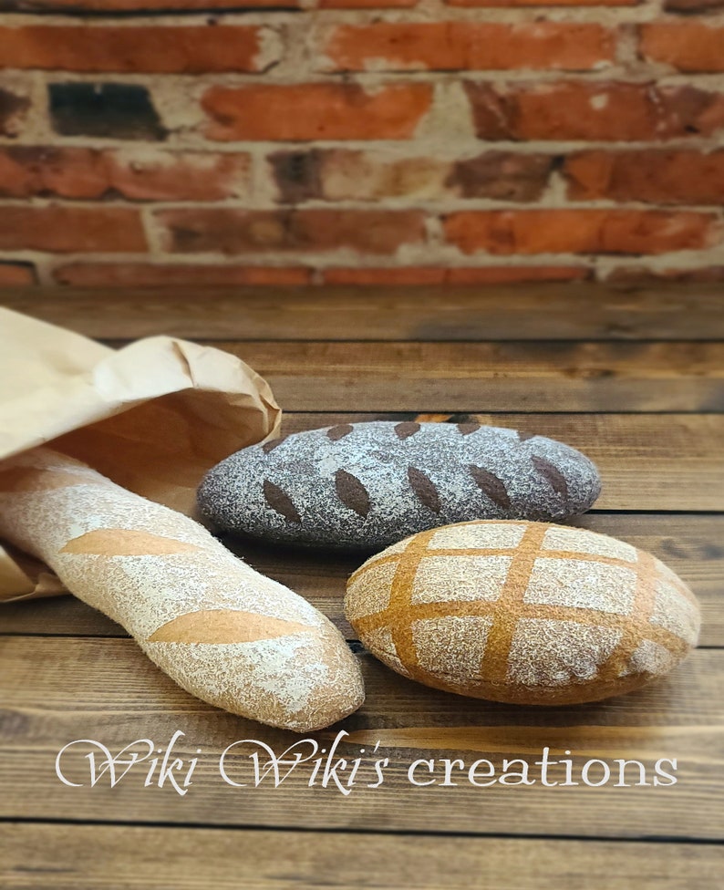 May include: Three felt loaves of bread on a wooden surface. The loaves are a light brown, dark brown, and a tan color. The loaves are decorated with different patterns. The text "Wiki Wiki's creations" is visible in the bottom right corner of the image.