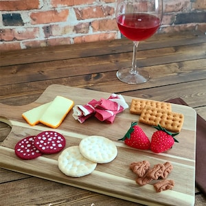 Könnte beinhalten: Ein Holzbrett mit einer Auswahl an Filzlebensmitteln, darunter Käse, Salami, Cracker, Erdbeeren und Speck. Das Brett liegt auf einem Holztisch mit einem Glas Rotwein im Hintergrund. "Wiki Wiki's creations" steht auf dem Brett.
