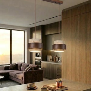 Peut inclure: Deux lampes suspendues modernes avec une finition marron et une section supérieure tachetée de couleur claire sont suspendues à une poutre en bois. Les lampes sont suspendues au-dessus d'un comptoir avec des tasses à café et une plante succulente.