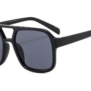May include: Black sunglasses featuring a square frame and dark grey lenses. The sunglasses have a double bridge design and thick arms. The overall style is modern and bold, suitable for various outdoor activities.