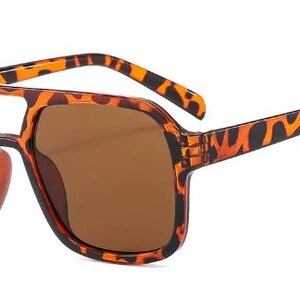 May include: Brown sunglasses with a tortoiseshell pattern on the frames and arms. The sunglasses have a double bridge design and brown tinted lenses. The overall shape is square and the style is retro.