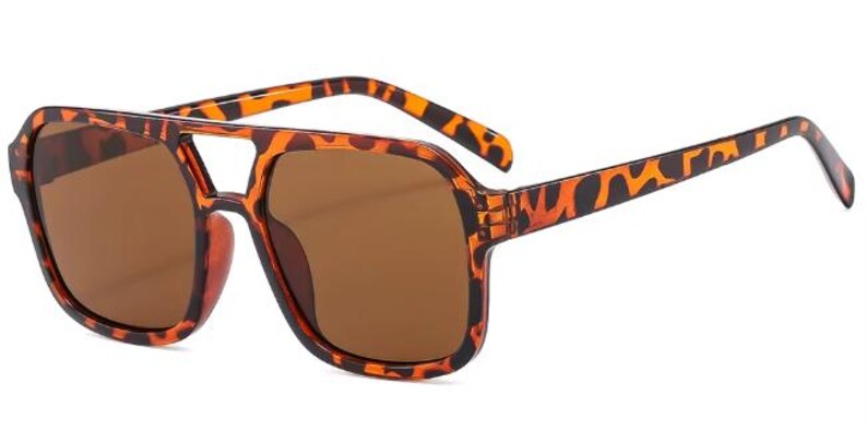 May include: Brown sunglasses with a tortoiseshell pattern on the frames and arms. The sunglasses have a double bridge design and brown tinted lenses. The overall shape is square and the style is retro.