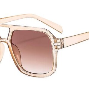 May include: Sunglasses with a beige frame and brown gradient lenses. The square-shaped sunglasses feature a double bridge and a light-coloured frame. The lenses transition from a darker brown at the top to a lighter brown at the bottom.