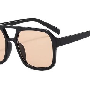 May include: Black square-framed sunglasses with a double bridge and light brown lenses. The sunglasses have a classic aviator style with a modern twist. The frames are thick and sturdy, providing a bold look.