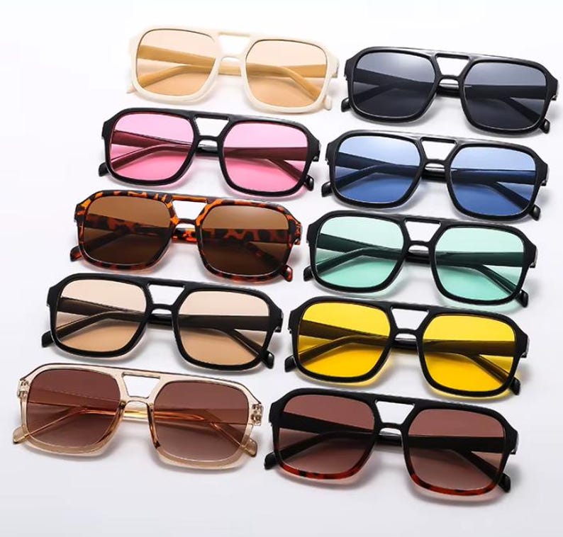 May include: An assortment of sunglasses with different coloured lenses, such as pink, blue, yellow, and brown. The frames are black, tortoiseshell, and cream. The sunglasses feature a double bridge design.