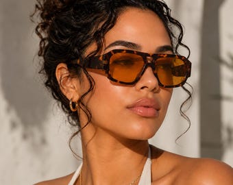 May include: Sunglasses with a thick, dark brown tortoiseshell frame and rectangular lenses in a vibrant amber orange tint. The eyewear features a prominent bridge and wide temples, providing a bold look with warm, translucent lens coloring.