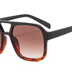 May include: Square-framed sunglasses with a black top bar and arms. The lenses are gradient brown, and the lower frame has a tortoiseshell pattern. These sunglasses offer a stylish, retro look.