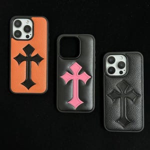 Puede incluir: Tres fundas para smartphone con un emblema de cruz en relieve. La funda de la izquierda es naranja con una cruz negra, la central es negra con una cruz rosa y la de la derecha es negra con una cruz negra. Acabado con textura.