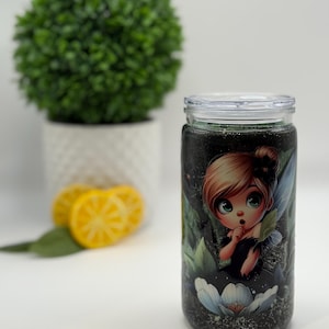 May include: A clear glass tumbler with a lid, featuring a cartoon fairy design. The fairy has blonde hair, blue wings, and is surrounded by a floral and leaf design. The tumbler is filled with a dark liquid and glitter.