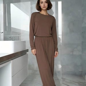 Op de afbeelding: Een effen bruine lounge set bestaande uit een top met lange mouwen en ronde hals en een bijpassende broek met wijde pijpen en een elastische tailleband. Het kledingstuk heeft een gladde, effen stoftextuur in een diepe, aardse bruine kleur.