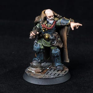 May include: Miniature figurine of a bald, bearded character in a detailed outfit. The figure is painted with a color palette of blue, green, brown, and tan. The character is standing on a circular base with a textured surface, pointing forward.