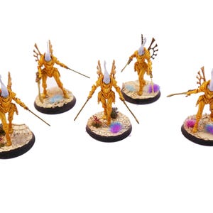 Può includere: Una collezione di sei miniature. Ogni figura indossa un'armatura dorata, impugna una spada e si erge su una base circolare. Le basi presentano un terreno desertico con accenti colorati. Le figure hanno un design unico e stilizzato.