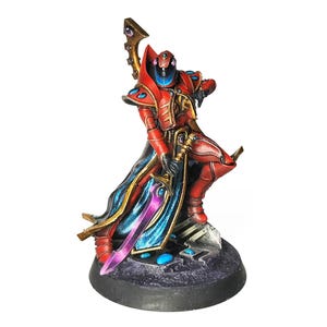 Peut inclure: Figurine miniature d'un guerrier en armure rouge avec des détails dorés, une cape bleue et dorée, et une épée violette. La figurine est posée sur une base texturée gris foncé.