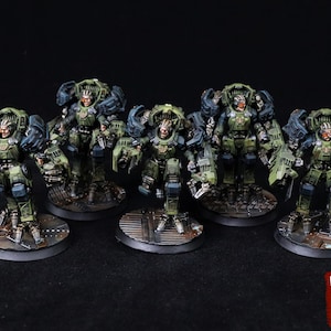 May include: Five miniature figures of soldiers in green and gray armor, each standing on a circular base. The figures have detailed mechanical components and are posed in a battle-ready stance. The background is black.
