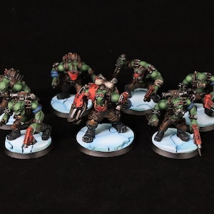 Puede incluir: Figuras en miniatura de orcos de piel verde con armaduras, armas y accesorios rojos y marrones. Los orcos están posados sobre bases circulares con efecto de nieve. La imagen incluye el texto "Creed's Painting".