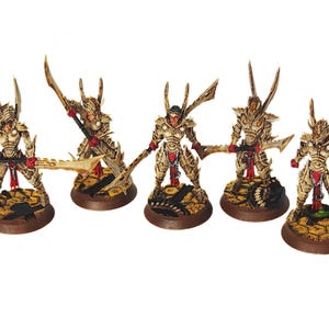 May include: Five miniature figurines of armored warriors with ornate gold and red detailing. Each figure stands on a textured brown base and wields a weapon. The warriors have helmets with tall, pointed features.