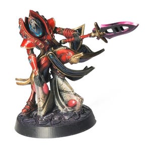 Könnte beinhalten: Miniaturfigur eines Kriegers in roter und goldener Rüstung, der ein Schwert und einen Schild hält. Die Figur hat einen blauen Helm und steht auf einem schwarzen Sockel. Die Schwertklinge ist rosa.