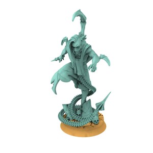 Puede incluir: Figura de color verde azulado claro de una figura humanoide con una larga túnica fluida y una cola de escorpión. La figura está posada dinámicamente, con una pierna levantada y los brazos extendidos. La base es de color beige con detalles de calaveras y huesos.