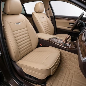 May include: A set of beige car seat covers with horizontal ribbed detailing on the backrests and seat cushions, featuring a small silver accent piece on the upper backrest, installed over the front seats and floor area of a vehicle interior.
