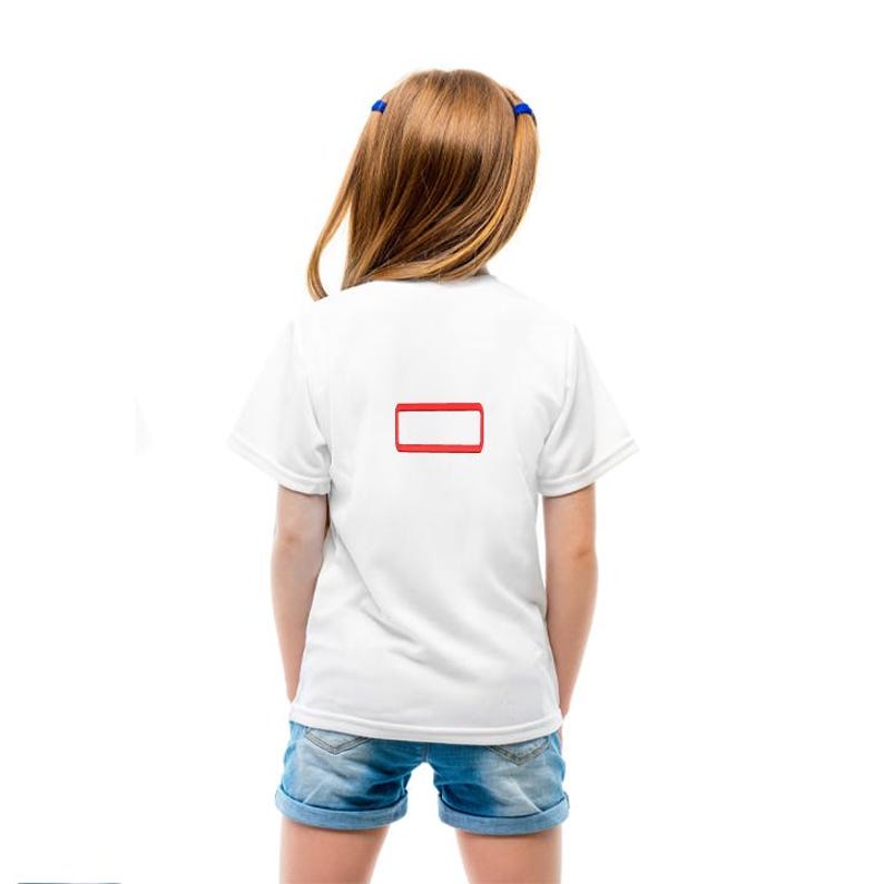 May include: A plain white short-sleeved t-shirt featuring a simple red rectangular outline graphic centered on the back. The garment is paired with blue denim shorts. The shirt has a standard crew neckline and a clean, minimalist design.