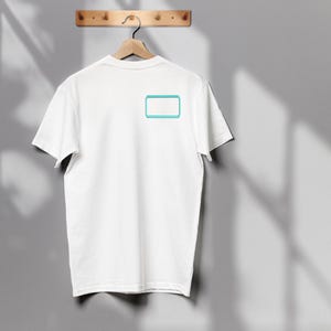 May include: A plain white short-sleeved t-shirt featuring a small, rectangular graphic on the upper left chest area. The graphic consists of a solid white center enclosed by a bright cyan blue border, creating a simple, clean, and minimalist design.