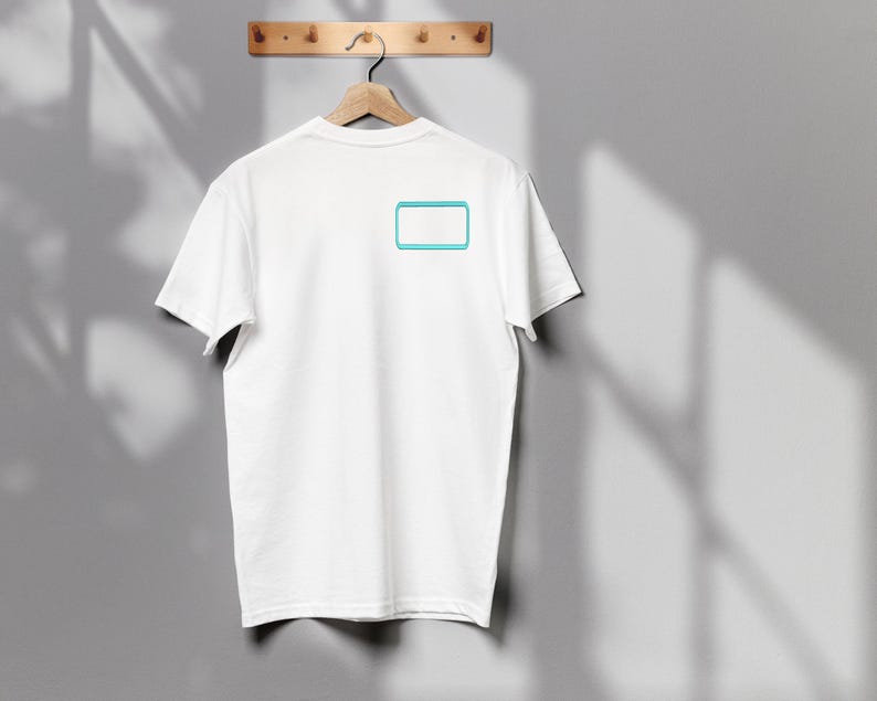 May include: A plain white short-sleeved t-shirt featuring a small, rectangular graphic on the upper left chest area. The graphic consists of a solid white center enclosed by a bright cyan blue border, creating a simple, clean, and minimalist design.