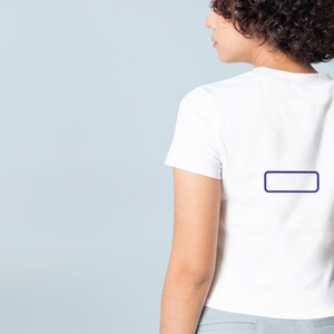May include: A plain white short-sleeved t-shirt featuring a small, empty dark blue rectangular outline centered on the upper back. The garment has a crew neckline and a fitted silhouette, shown from a rear-facing perspective against a light blue background.