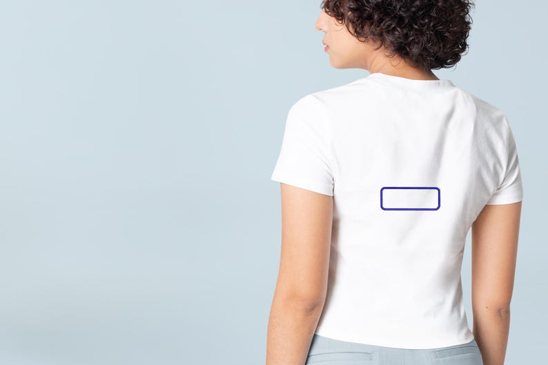 May include: A plain white short-sleeved t-shirt featuring a small, empty dark blue rectangular outline centered on the upper back. The garment has a crew neckline and a fitted silhouette, shown from a rear-facing perspective against a light blue background.