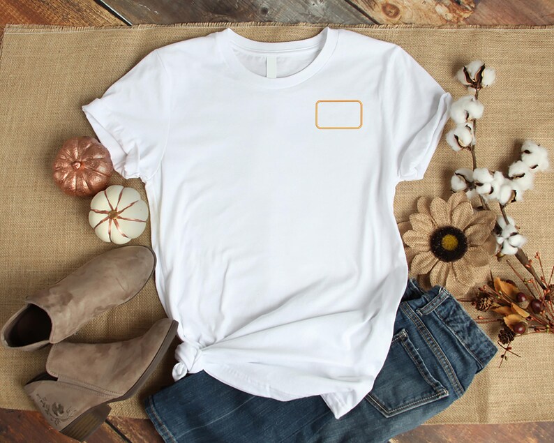 May include: A white short-sleeved t-shirt featuring a blank, rectangular orange outline on the upper left chest area. The shirt has a crew neckline and is displayed flat with a knotted hem detail on the lower left side of the garment.