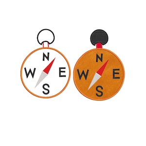 May include: Two circular embroidered compass patches featuring black cardinal direction letters N, E, S, and W. One patch has a white background, the other has a tan background. Both include a red and white needle and a black circular attachment loop.