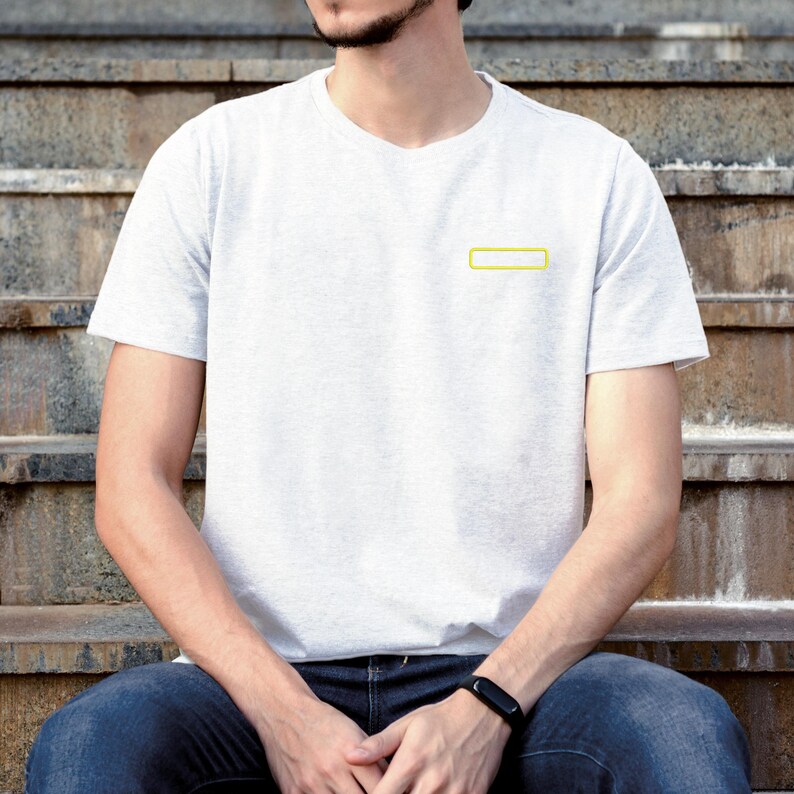 May include: A light gray short-sleeved t-shirt featuring a small, rectangular yellow outline graphic on the left chest. The shirt has a crew neckline and a plain, solid-colored back, providing a simple and clean appearance for casual wear.