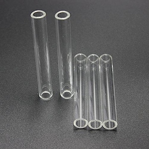 May include: Clear glass test tubes with rounded bottoms and open tops are arranged on a dark surface. Two tubes stand upright, while three are grouped together. The tubes are cylindrical and appear to be made of transparent glass.