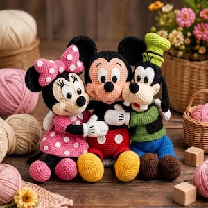 May include: Three crocheted dolls featuring Minnie Mouse in a pink polka-dot dress with a matching bow, Mickey Mouse in red shorts with white buttons, and Goofy in a green sweater, black vest, blue pants, and a green hat, all hugging together.