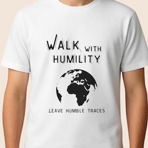 Könnte beinhalten: Eine weiße Keramiktasse mit schwarzem Henkel und dem Text "But First, Coffee" in fetter, schwarzer Schrift. Die Tasse steht vor einem verschwommenen Hintergrund, der eine gemütliche Umgebung suggeriert.