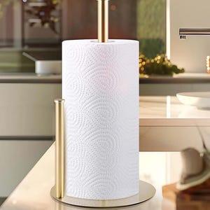 May include: A gold-colored paper towel holder with a full roll of white paper towels. The holder has a circular base and a vertical rod to hold the roll in place. The design is simple and modern, suitable for a kitchen.