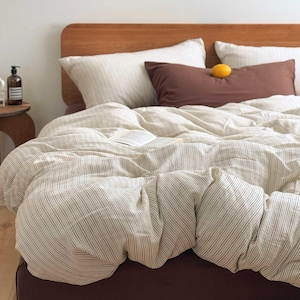 May include: A bed with a wooden headboard and a cream-colored striped duvet cover. Two white striped pillows and a brown pillow are on the bed. A lemon rests on the brown pillow. A book is open on the bed.